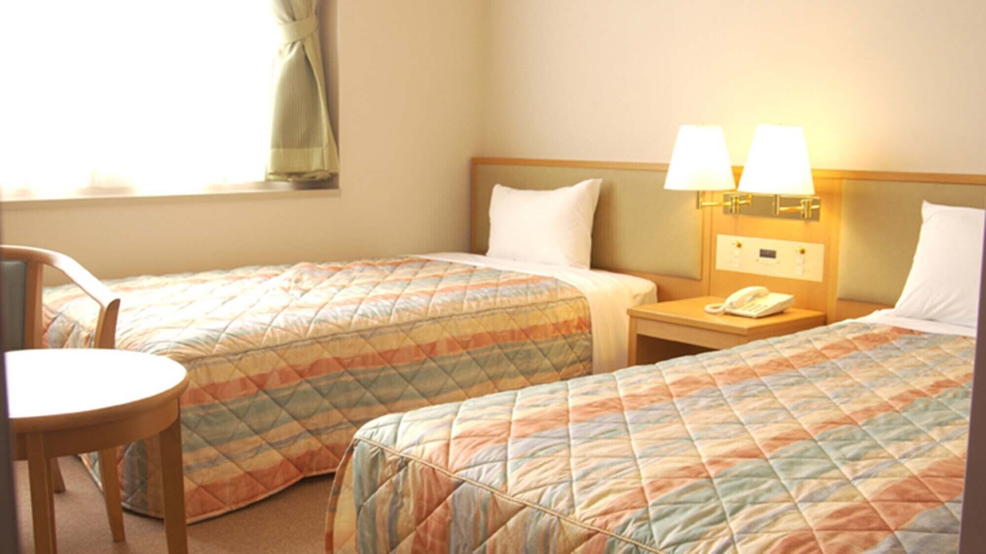 Habitació d'hotel amb dos llits, una taula de nit amb un telèfon, una cadira i una finestra amb cortines.