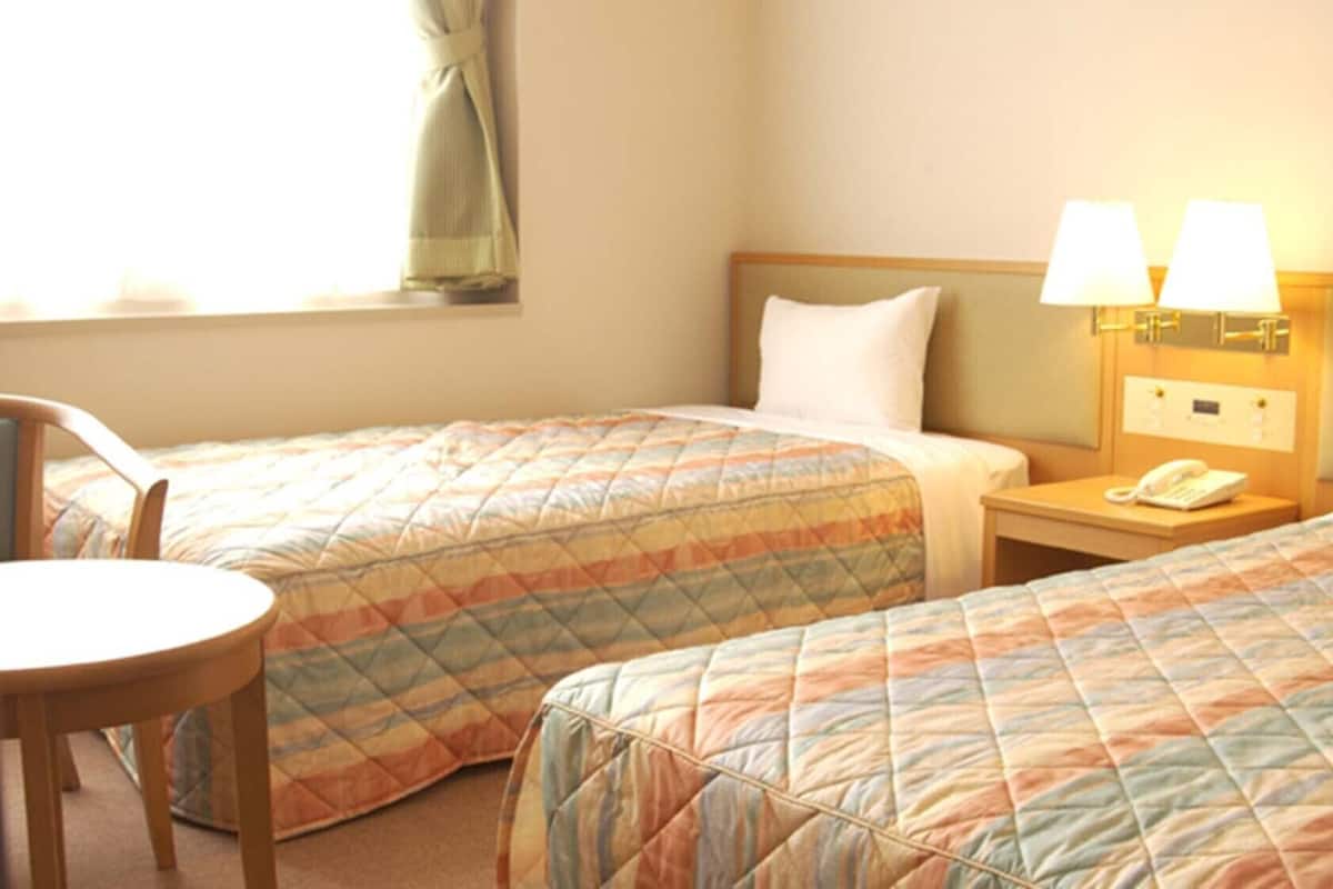 A hotel room with two beds, a nightstand with a phone, a chair, and a window with curtains.