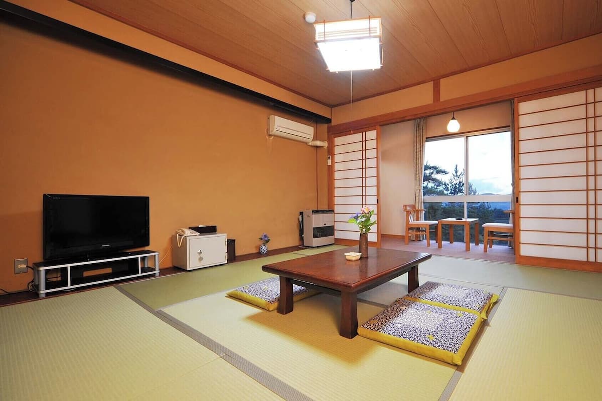 A traditional Japanese room with tatami flooring, a television, a heater, and a sliding door leading to a balcony.