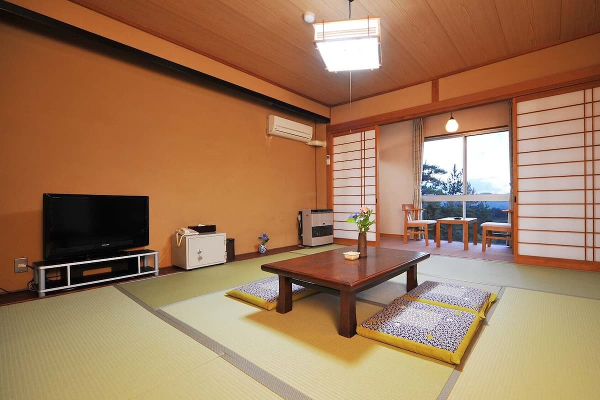 A traditional Japanese room with tatami flooring, a television, a heater, and a sliding door leading to a balcony.