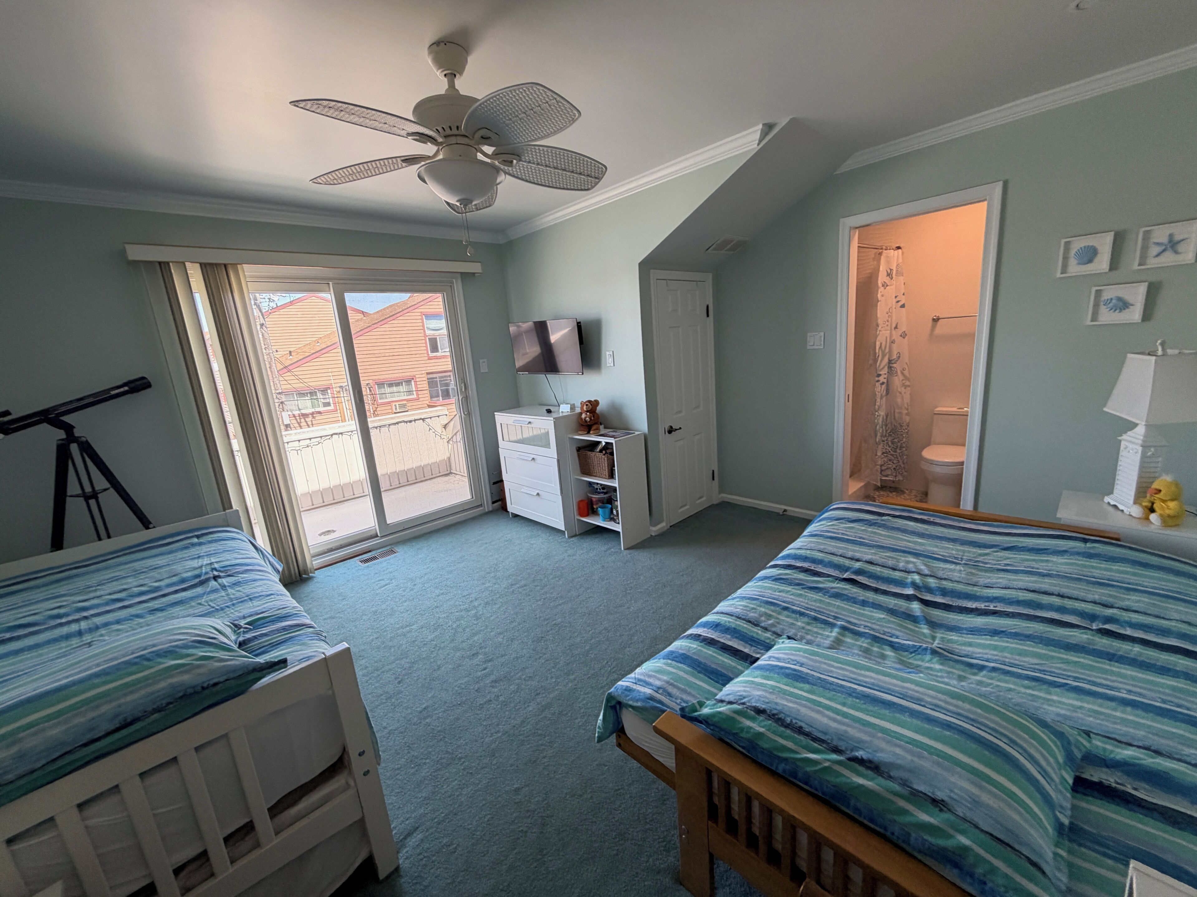 A bedroom with two beds, a ceiling fan, a TV, and a sliding glass door to the outside.