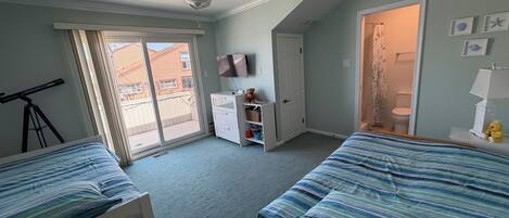 A bedroom with two beds, a ceiling fan, a TV, and a sliding glass door to the outside.