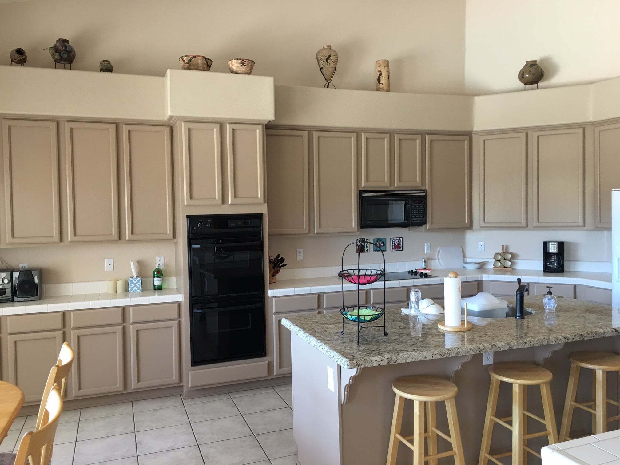 A kitchen with beige cabinetry, a black oven, a microwave, a granite countertop, and wooden stools.