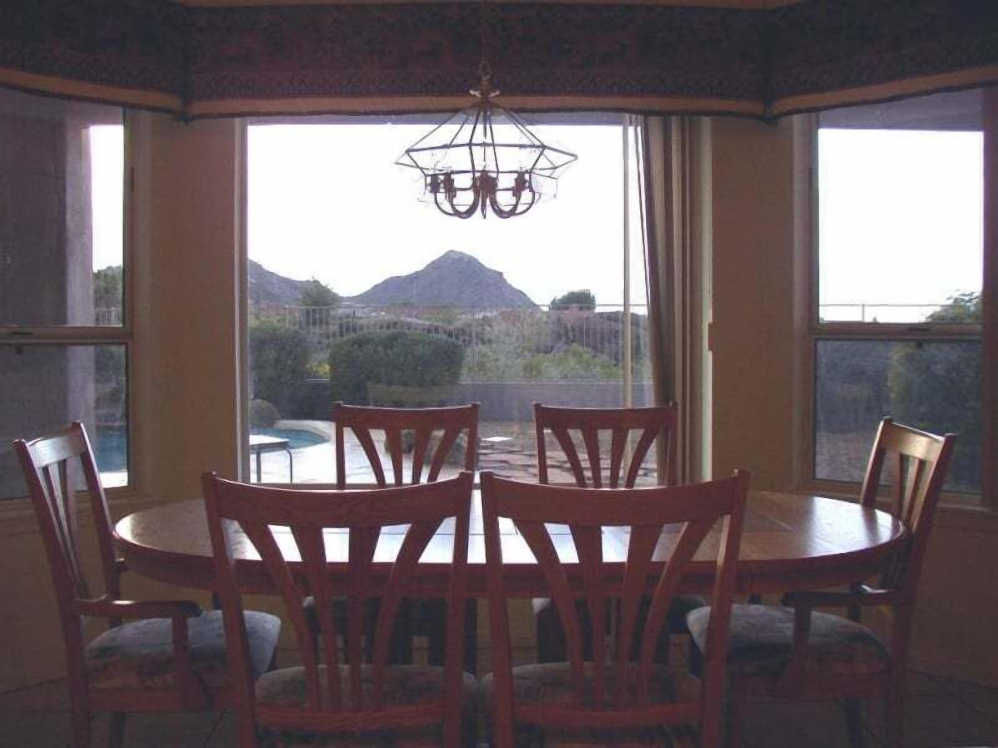A dining area with a round table and six chairs, large windows with a view of mountains, and a chandelier.