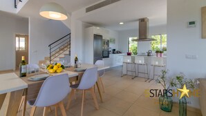 Uma cozinha moderna com armários brancos, eletrodomésticos de aço inoxidável e uma área de jantar com mesa posta para dois.