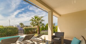 An outdoor patio area with wicker furniture, a glass table, and a pool. - Brisa de Mar 1, Villa 5StarsHome Mallorca (Alcúdia)