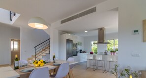 A modern kitchen with white cabinets, stainless steel appliances, and a dining area with a table set for two. - Brisa de Mar 1, Villa 5StarsHome Mallorca (Alcúdia)