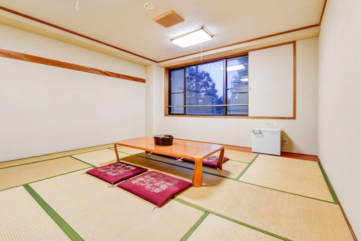 A tatami mat room with a low table, cushions, a window, and a small refrigerator.