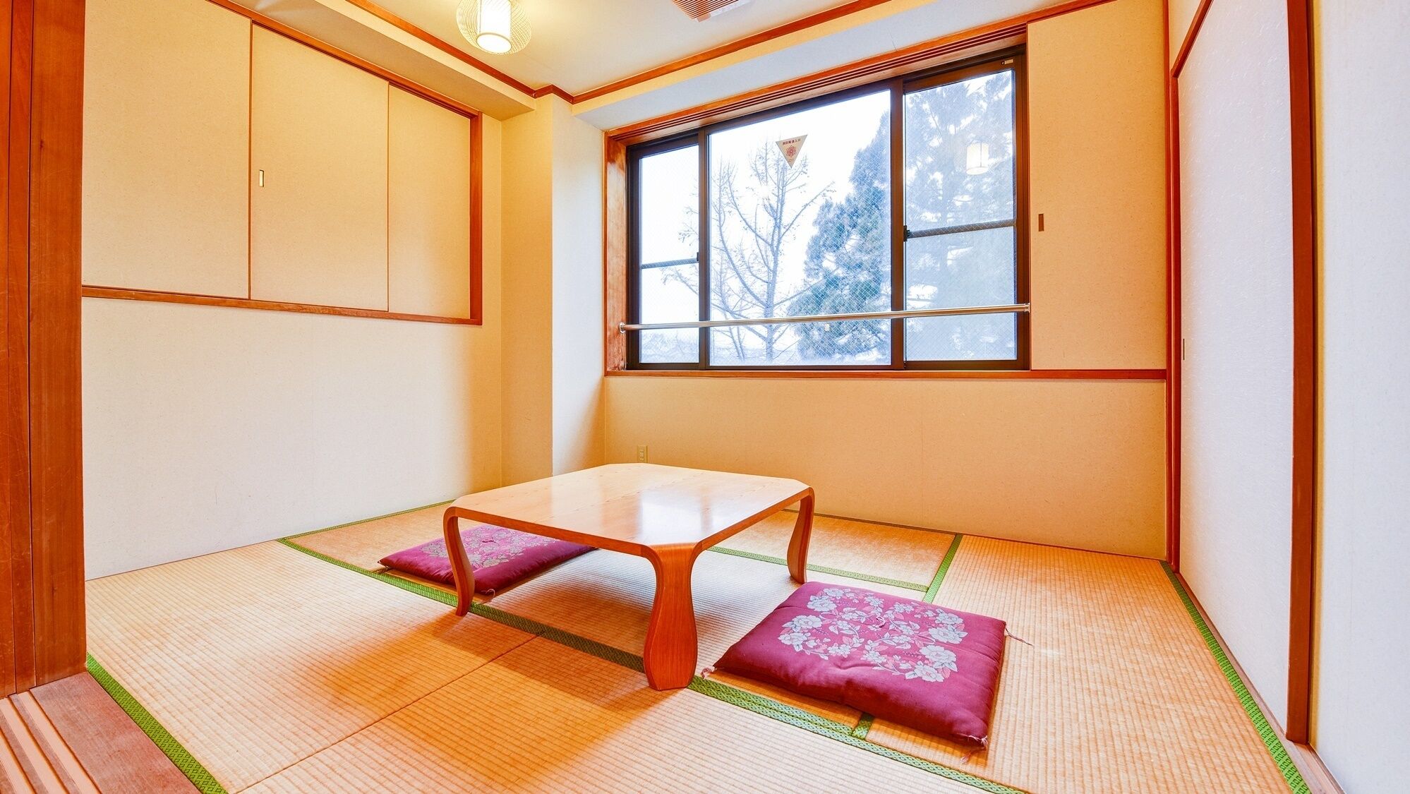 A traditional Japanese room with tatami flooring, a low wooden table, and a window with a view of trees.