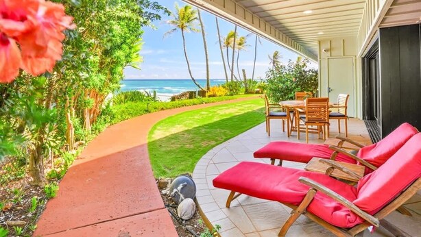 A covered outdoor area with a view of the ocean, a lawn, and a dining table with chairs. - Aloha Manor is Elegant Gated Oceanfront Living! (Kapaʻa)