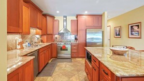 A kitchen with wooden cabinets, a stainless steel range hood, a double oven, a refrigerator, and granite countertops. - Aloha Manor is Elegant Gated Oceanfront Living! (Kapaʻa)