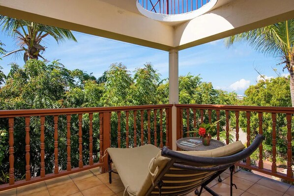 A balcony with a wooden railing, a cushioned chair, and a small table with a vase of flowers.