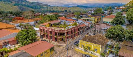 A multi-story hotel with a red facade, located in a hilly town with visible railway tracks and greenery.