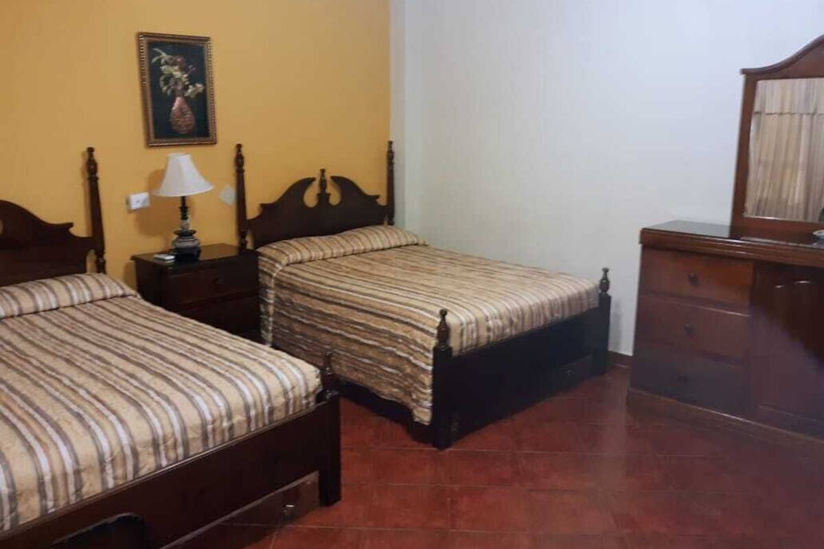 A bedroom with two beds, a nightstand, a dresser, and a mirror.