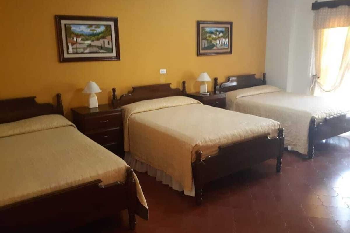A hotel room with three wooden beds, each with a matching nightstand and lamp.