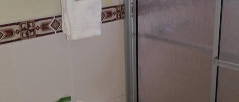 Un baño con inodoro, cabina de ducha y estante con toallas dobladas.