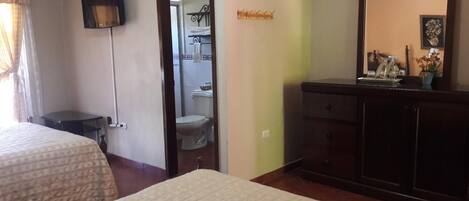 Une chambre d’hôtel avec deux lits, une commode en bois foncé, un miroir et une salle de bain visible à travers une porte ouverte.