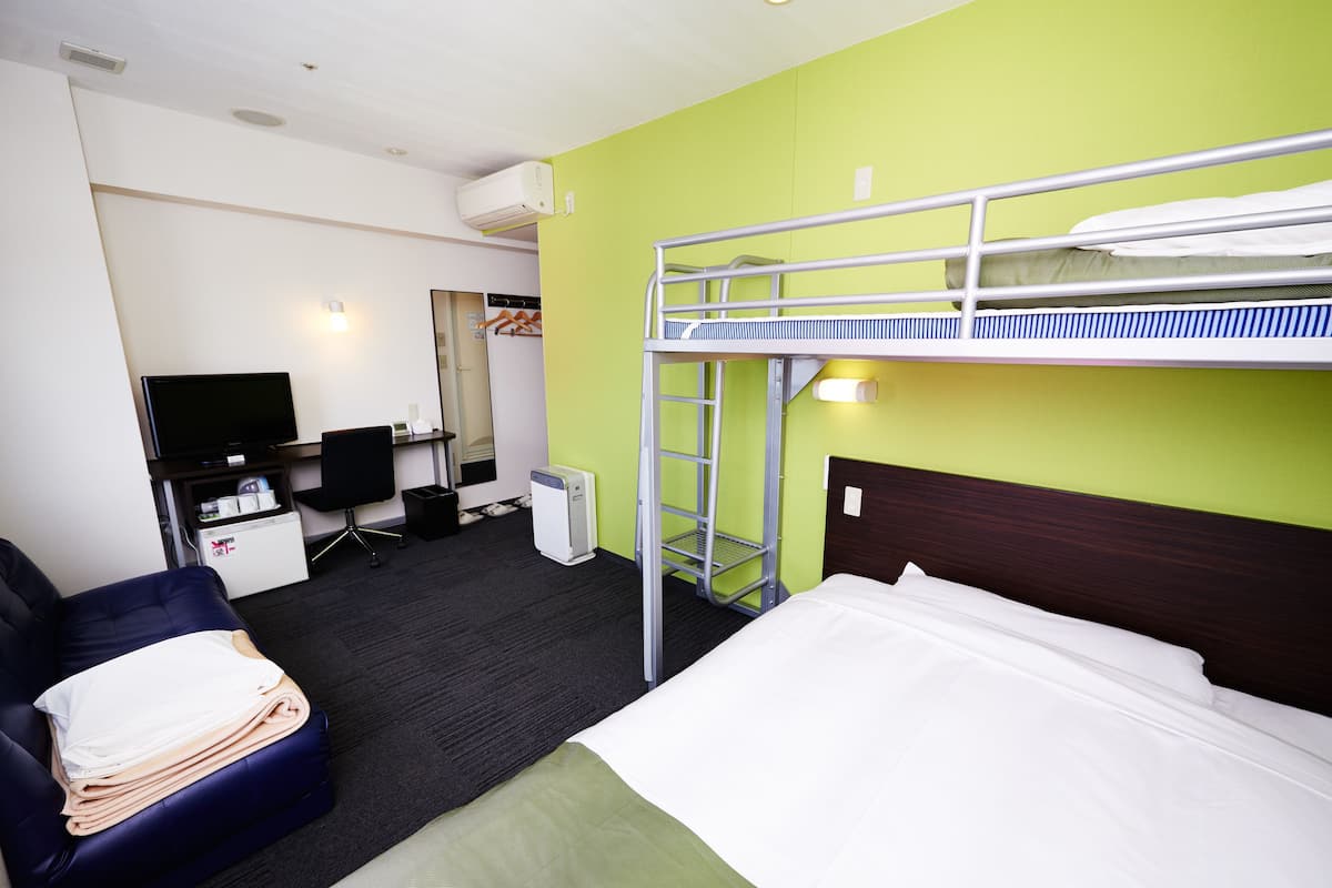 A hotel room with bunk beds, a desk, a chair, a television, and a small refrigerator.