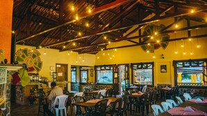 Un restaurante con vigas de madera, luces colgantes y mesas con sillas.
