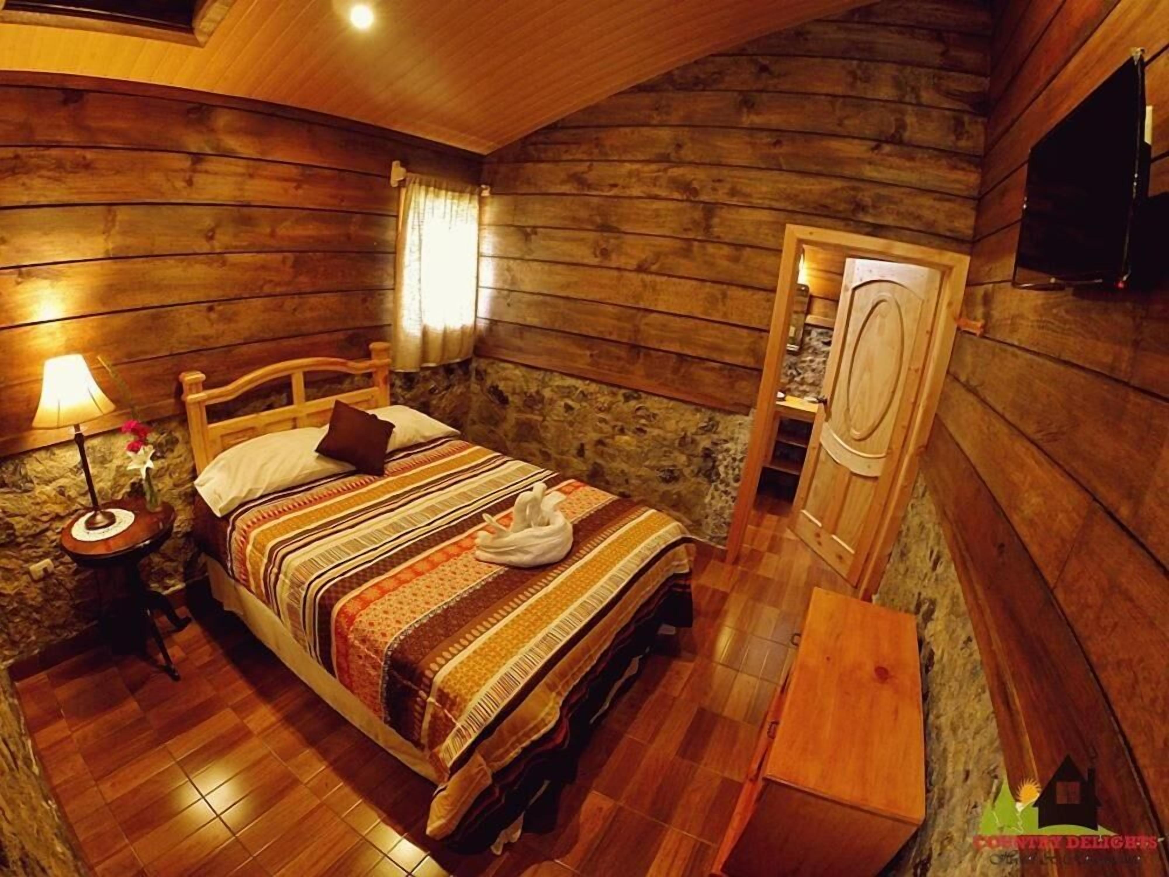 Un dormitorio rústico de cabaña con una cama de madera, una mesita de noche con lámpara y una pared de piedra.