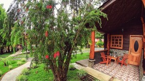 Una casa de madera con un patio empedrado, un pequeño jardín con diversas plantas y un sendero que lleva a la casa.