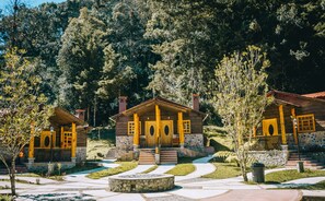 A row of wooden cabins with stone steps leading up to the entrance, surrounded by a landscaped garden and dense forest. - Country Delights Hotel (Purulha)