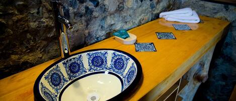 A bathroom with a stone wall, a wooden countertop, a sink with blue and white tiles, a faucet, and a towel on the counter.