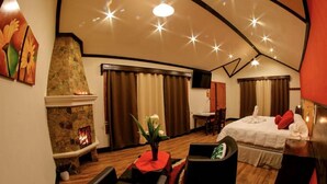 Una habitación de hotel acogedora con chimenea de piedra, una cama con almohadas rojas y un comedor con mesa y sillas.