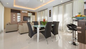 A modern living room with a glass dining table, black chairs, a sofa, and a kitchen area with a bar counter. - The Reiko Villa Bali (Nusa Dua)
