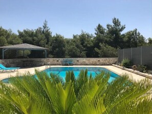 A rectangular swimming pool with a stone wall and a covered seating area.