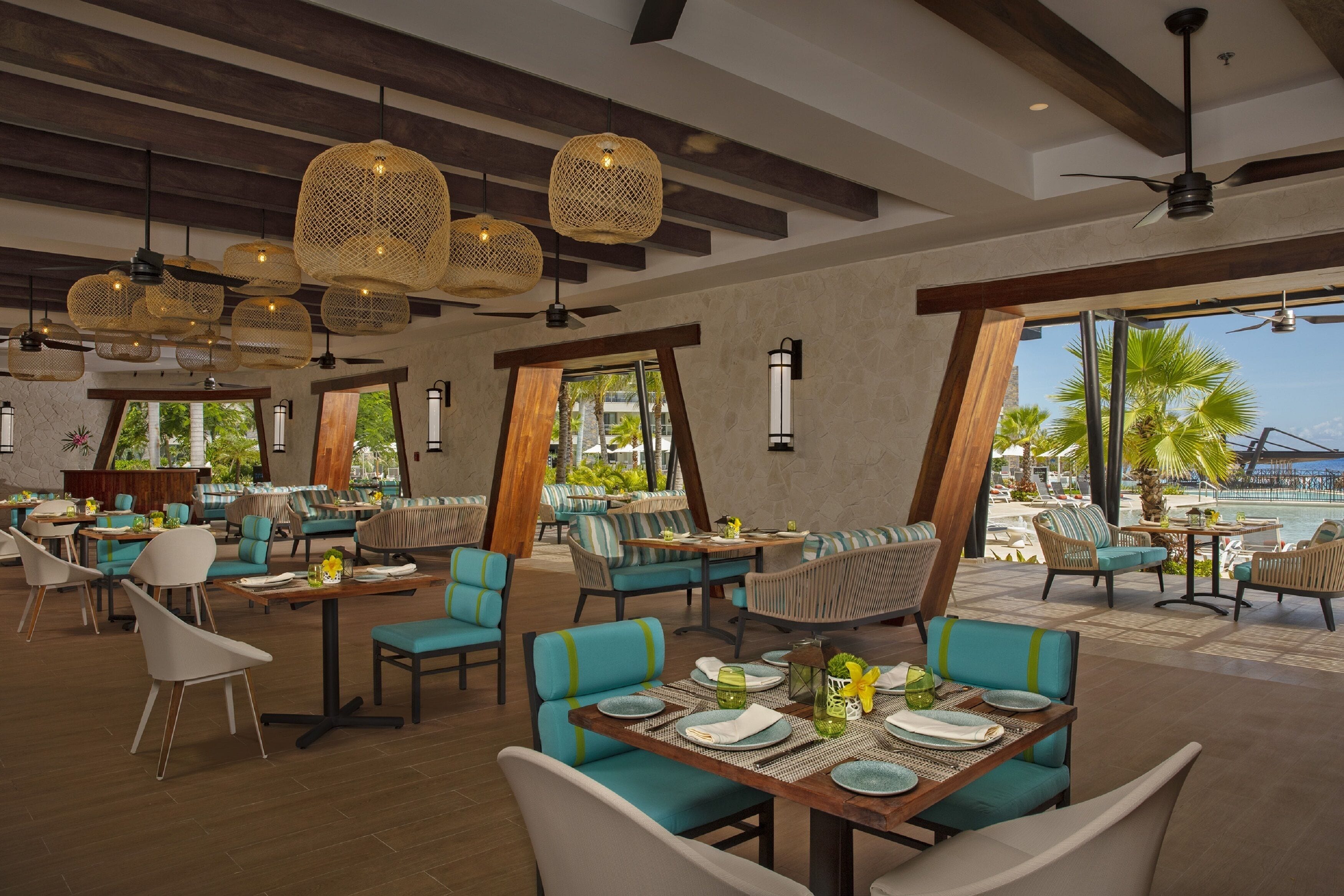 A restaurant with tables and chairs, large windows, and hanging lights.