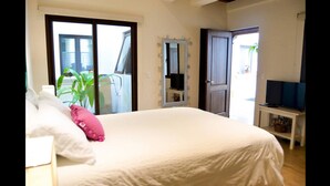 A bedroom with a large bed, a mirror with lights, a TV, and a balcony with plants. - Casa Girasol (Antigua Guatemala)