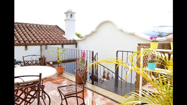A patio with a round table and chairs, potted plants, and a metal railing. - Casa Girasol (Antigua Guatemala)