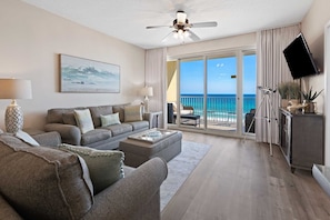 A spacious living room with a grey sofa, a coffee table, and a large window offering a view of the ocean.