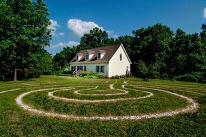A white house with a symmetrical garden maze in front.