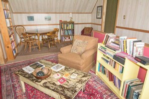 A cozy room with a round table, chairs, a sofa, a bookshelf, and a coffee table with books and decorative items. - 11-Acres | Groups | Fire Pit | Wooded Retreat (Gold Hill)