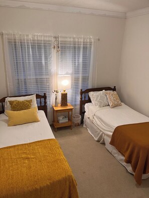 A room with two beds, a bedside table with a lamp, and a window with curtains. - 11-Acres | Groups | Fire Pit | Wooded Retreat (Gold Hill)