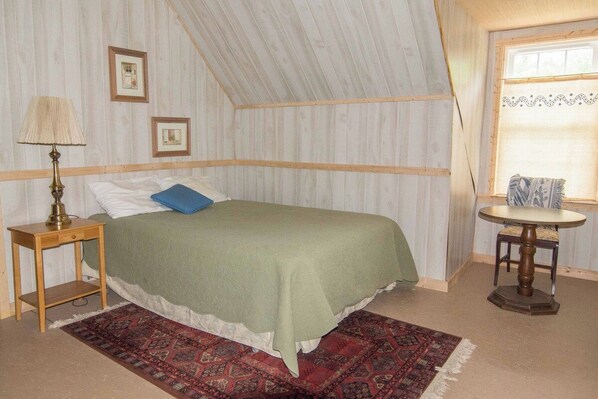 Une pièce comprenant un lit, une petite table, une lampe, une fenêtre et un tapis à motifs.