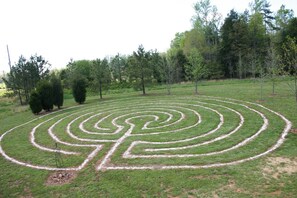 Un ampio giardino labirintico a forma di cerchio, con un palo al centro, circondato da un prato e alberi.