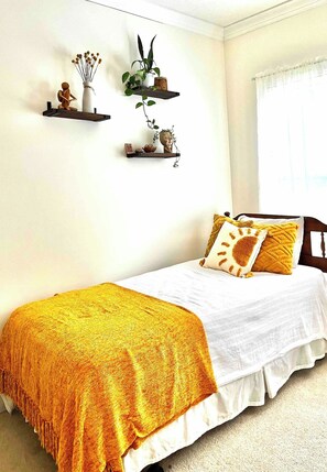 Una camera da letto con un letto, una coperta gialla e mensole a parete con oggetti decorativi.