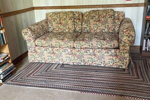 A floral-patterned sofa in a corner of a room with a bookshelf and a patterned rug.