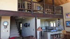 A spacious living area with a high ceiling, a staircase leading to a loft, and a kitchen with white cabinets and a central island. - Rustic mountain home with stunning mountain views from the large deck! (Crested Butte)