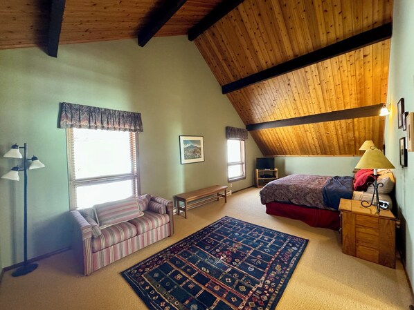 A cozy attic bedroom with a sloped ceiling, a bed, a bench, a sofa, and a rug.