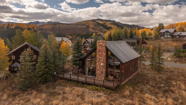 A lodge with a stone chimney, large windows, and a deck overlooking a mountainous area. - Rustic mountain home with stunning mountain views from the large deck! (Crested Butte)