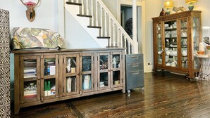 A spacious living area with a wooden cabinet, a staircase, and a glass-fronted cabinet with shelves.