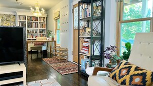 A living room with a TV, sofa, and bookshelf. There is a dining area with a table and chairs.