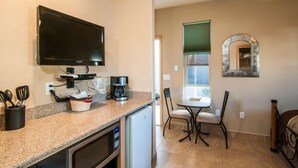 A compact kitchen with a microwave, coffee maker, and a TV mounted above the counter. There is a dining area with a table and chairs, and a small mirror on the wall. - Separate Private Detached 1 Room Casita with your own entrance (Albuquerque)