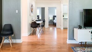 A spacious living area with a dining table and chairs, a TV, and a kitchen area in the background.