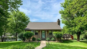 A single-story house with a front porch, a stone chimney, and a well-maintained lawn.