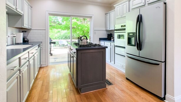 A modern kitchen with white cabinets, stainless steel appliances, and a wooden floor.